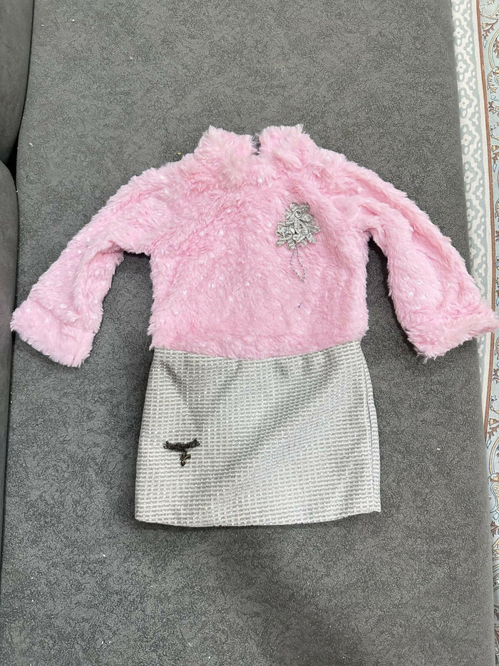 Pink fuzzy sweater and white skirt with black pattern on a gray surface