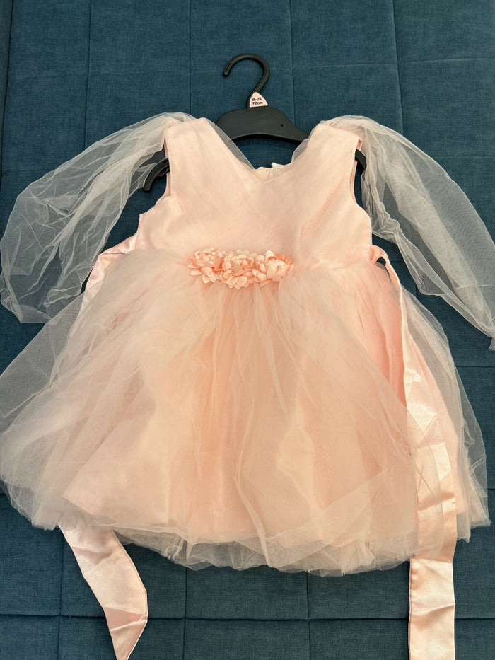 Pink dress with sheer sleeves on a hanger against a blue textured background