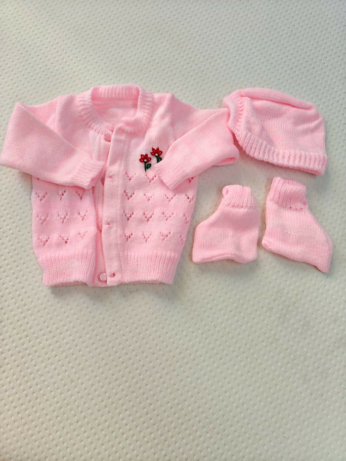 Pink baby cardigan, hat, and booties set on a textured surface