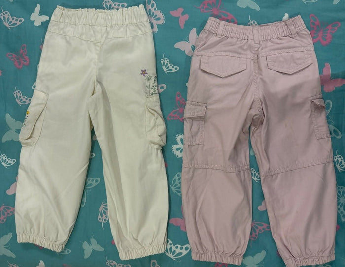 Two pairs of pants, one beige and one pink, on a blue floral-patterned surface.
