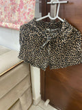 Leopard print shorts hanging on a hanger against a floral curtain background.