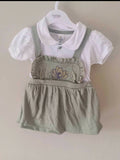 Children's outfit with white shirt and green overalls on a hanger against a beige background