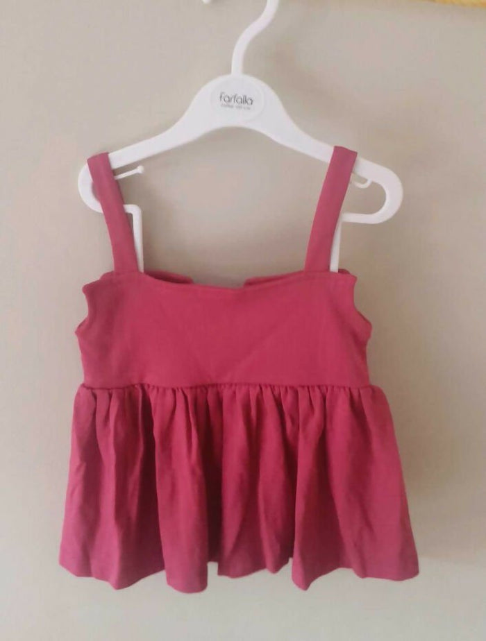 Pink tank top with straps on a white hanger against a beige background