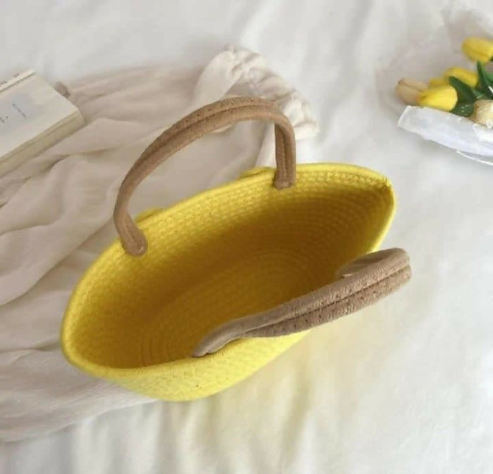 Yellow woven handbag with brown handles on a light background