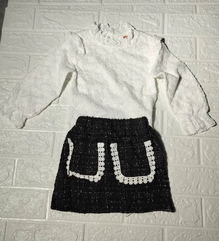 White blouse with long sleeves and a black skirt with white patterns