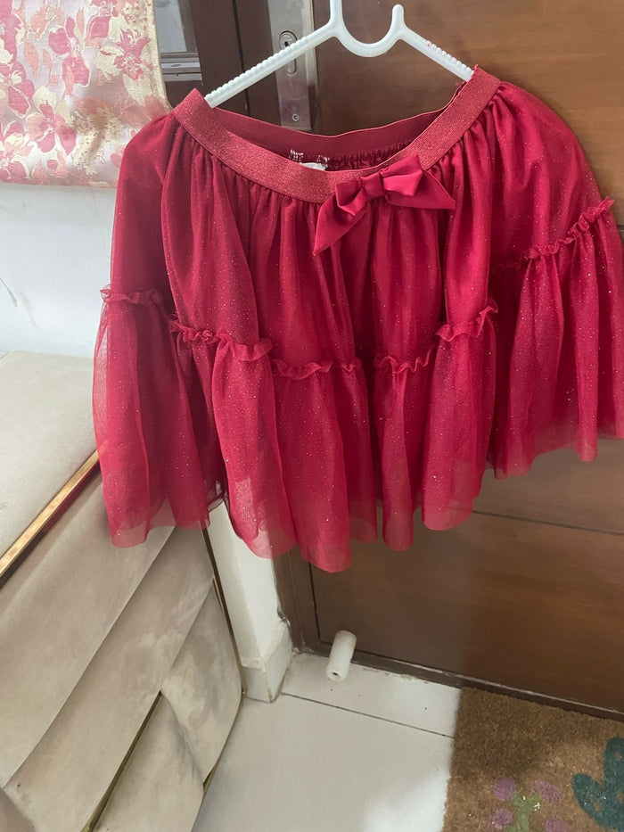 Red blouse with ruffled sleeves and a bow on a hanger against a wooden door.