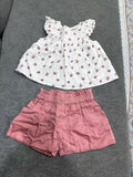 White floral top and pink shorts set on a gray surface