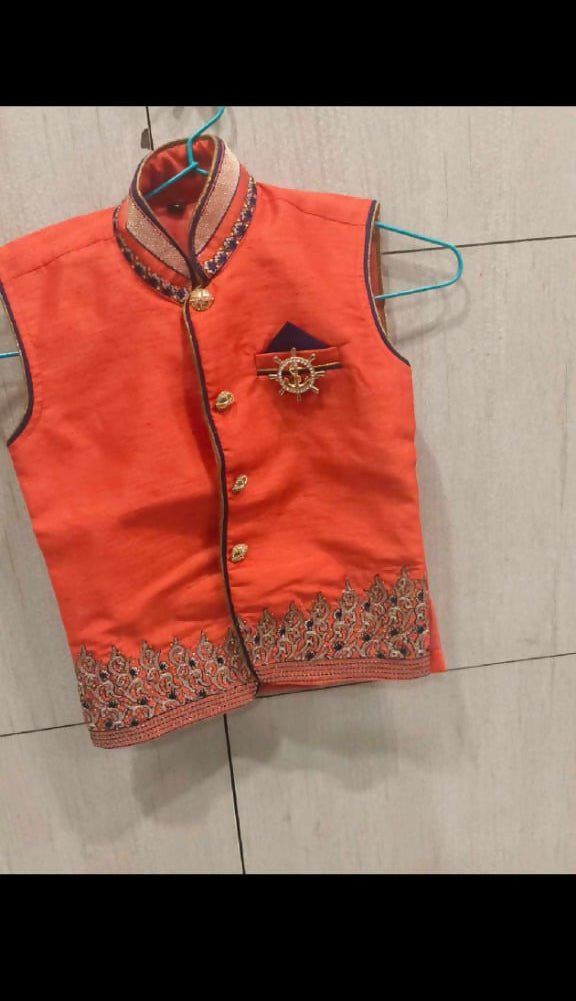 Orange embroidered vest on a hanger against a tiled wall background