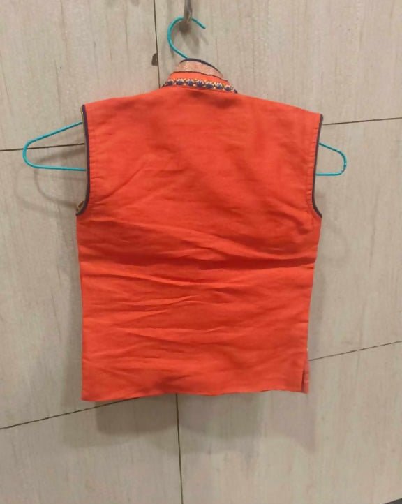 Orange sleeveless shirt on a hanger against a tiled wall