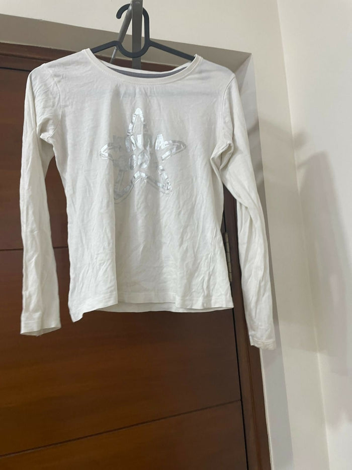 White long-sleeve shirt with a logo on a hanger against a wooden door.