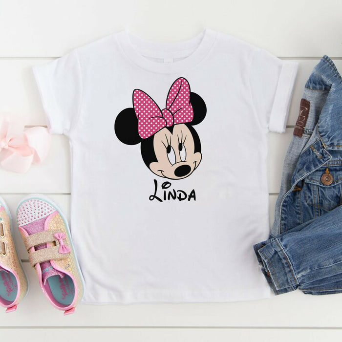 White t-shirt with Minnie Mouse design and name 'Linda', paired with denim jacket and shoes on a light wooden surface.