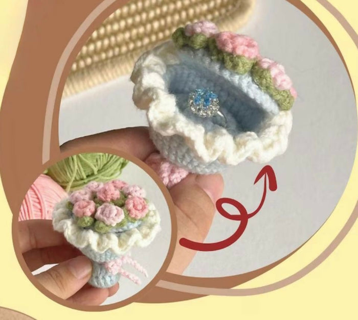 Decorative crochet flower pot with pink flowers held by a hand, on a light background.